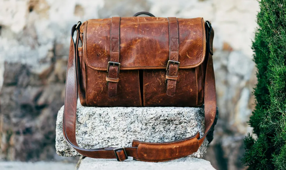 Brown leather satchel bag on gray concrete surface near green plant at daytime