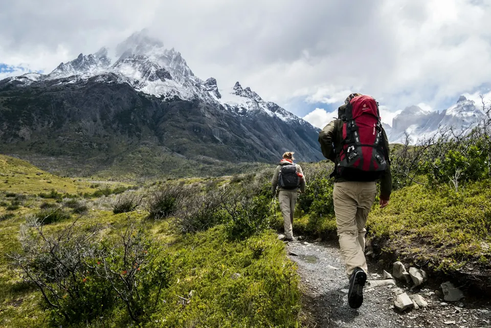 Two hikers with backpacks walking toward mountains