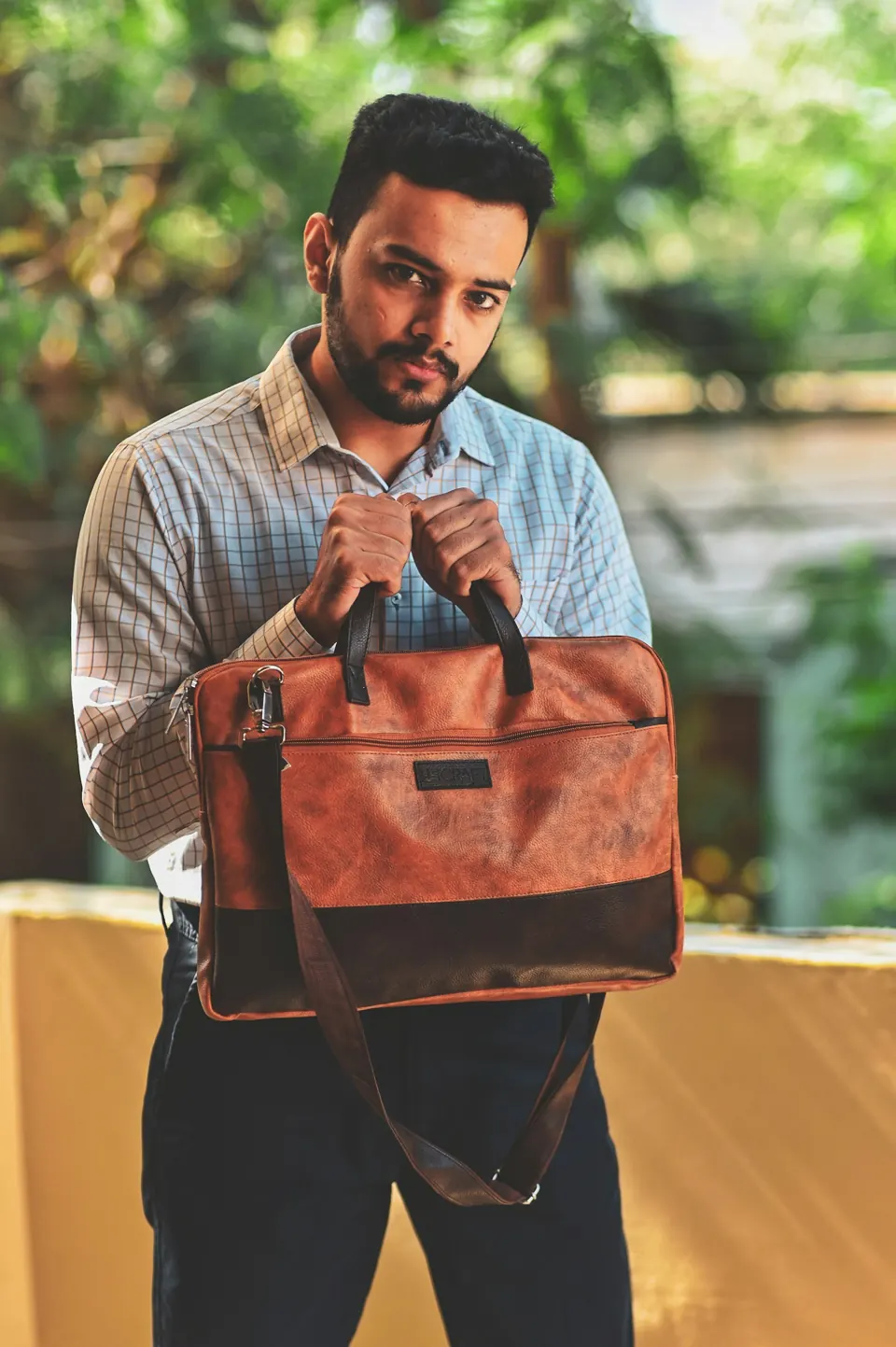 Man in blue and white plaid button up shirt with brown leather sling bag