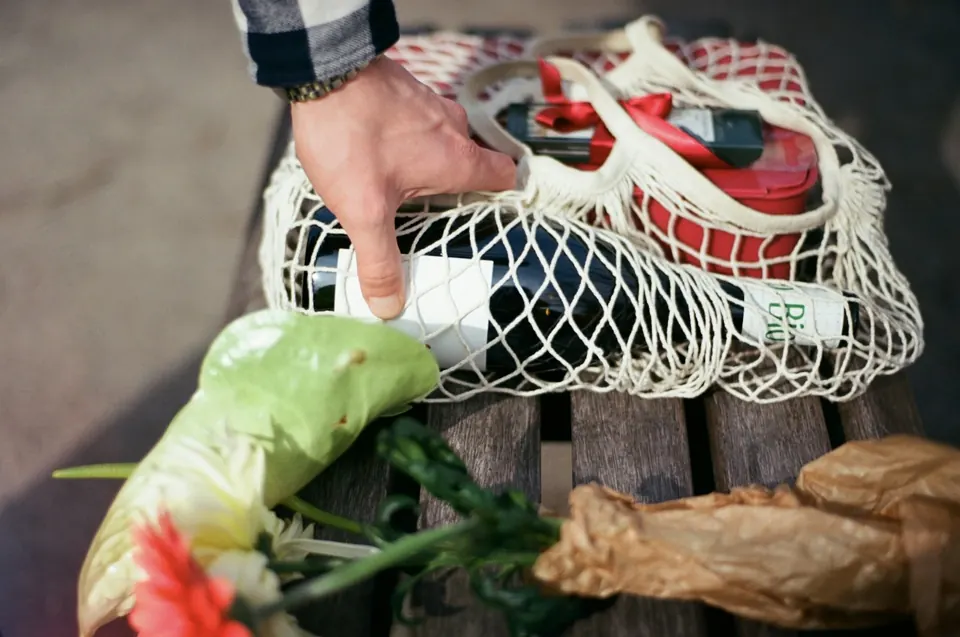 Hand placing wine bottle into reusable grocery bag