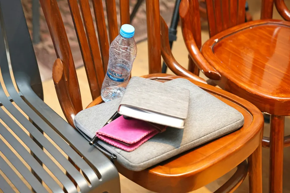 A grey laptop sleeve, notebook, and pink wallet on a wooden chair